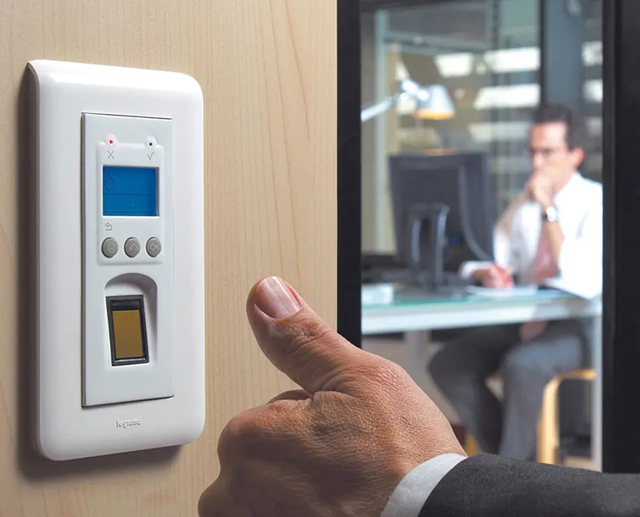 A person’s hand reaching towards a digital control panel mounted on a wall