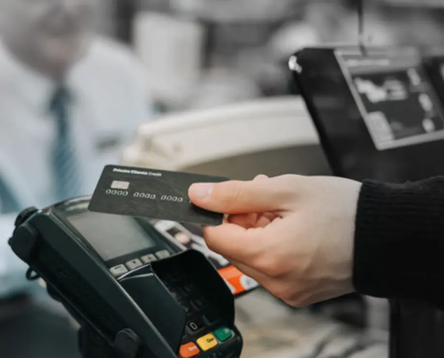 A person holding a credit card near a payment terminal in a retail environment.
