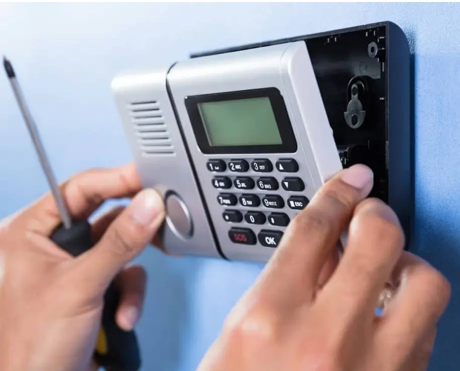 A person is installing a security system keypad on a wall, using a screwdriver.