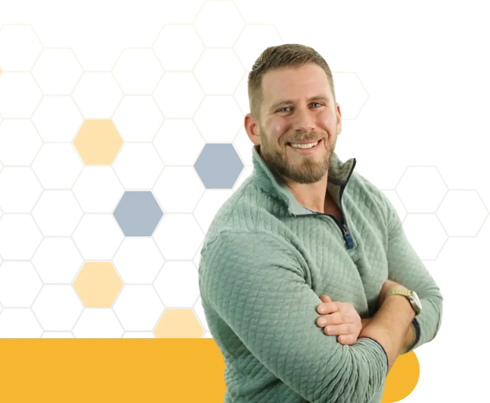 A man smiling, wearing a light green sweater, with his arms crossed against a geometric background of hexagons.