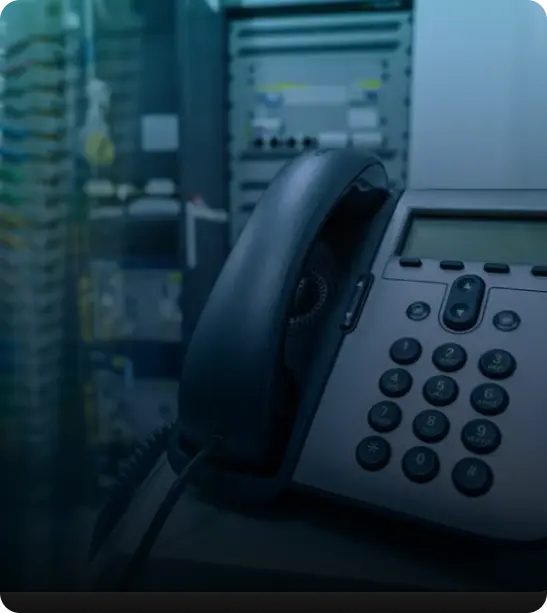 A close-up of an office telephone in front of blurred equipment in a server room.