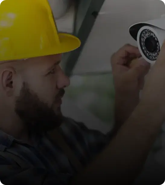A worker in a yellow hard hat is installing a security camera.