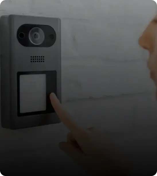 A person pressing a button on a wall-mounted intercom or video doorbell.