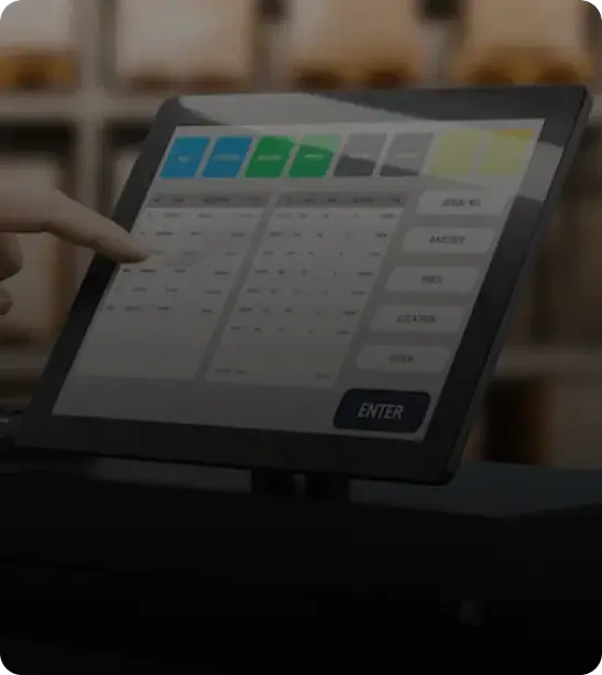 A close-up of a person's hand pointing at a touchscreen interface displaying various buttons and a data entry grid.