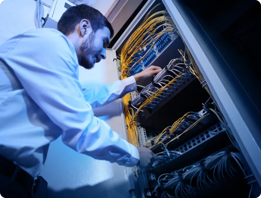 A technician working on a network server rack, adjusting cables and equipment in a data center.