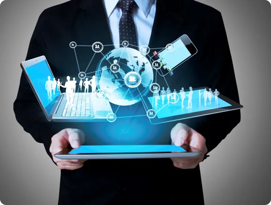 A person in a suit is holding multiple digital devices displaying holographic images of the globe and people interconnected through technology.