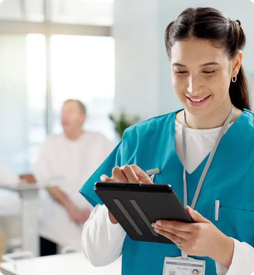 A healthcare professional smiling and using a tablet in a clinical setting.