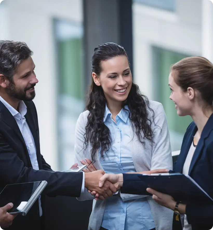 A group of three professionals in business attire engaging in a handshake and discussion in an office setting.