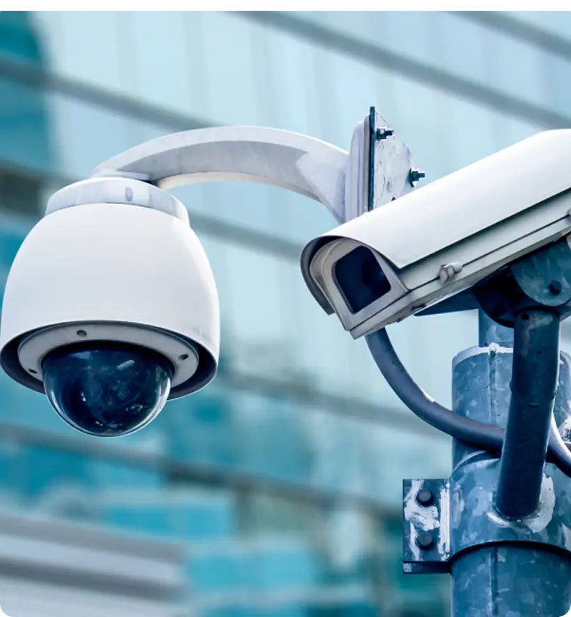 Security cameras mounted on a pole with a blurred modern building in the background.