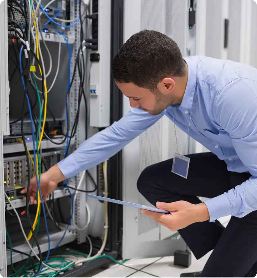 A technician working on network servers in a data center, adjusting cables and equipment.