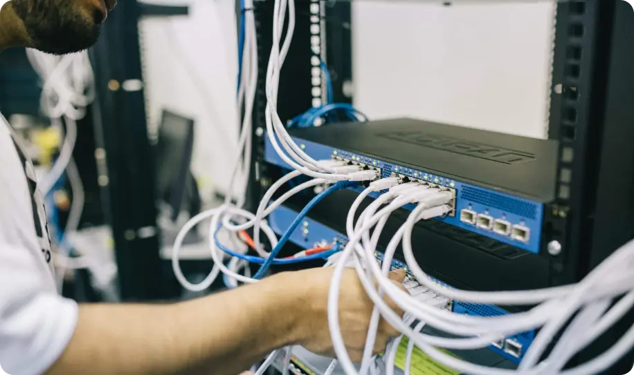 A person working on network equipment with cables.