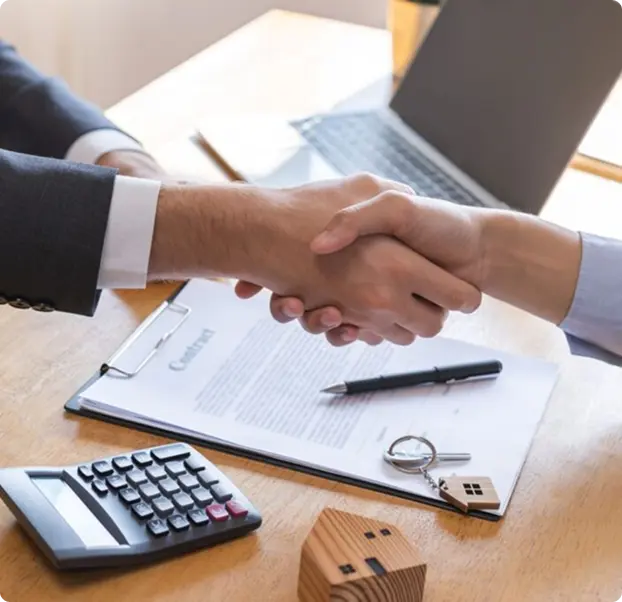 A close-up of two people shaking hands over a wooden table with a document