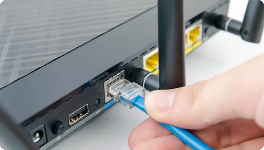 A close-up of a person's hand connecting an Ethernet cable to the back of a router
