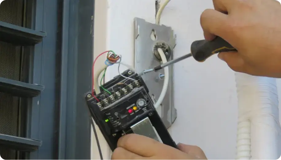 A person using a screwdriver to work on an electrical panel with wires and a device in hand.