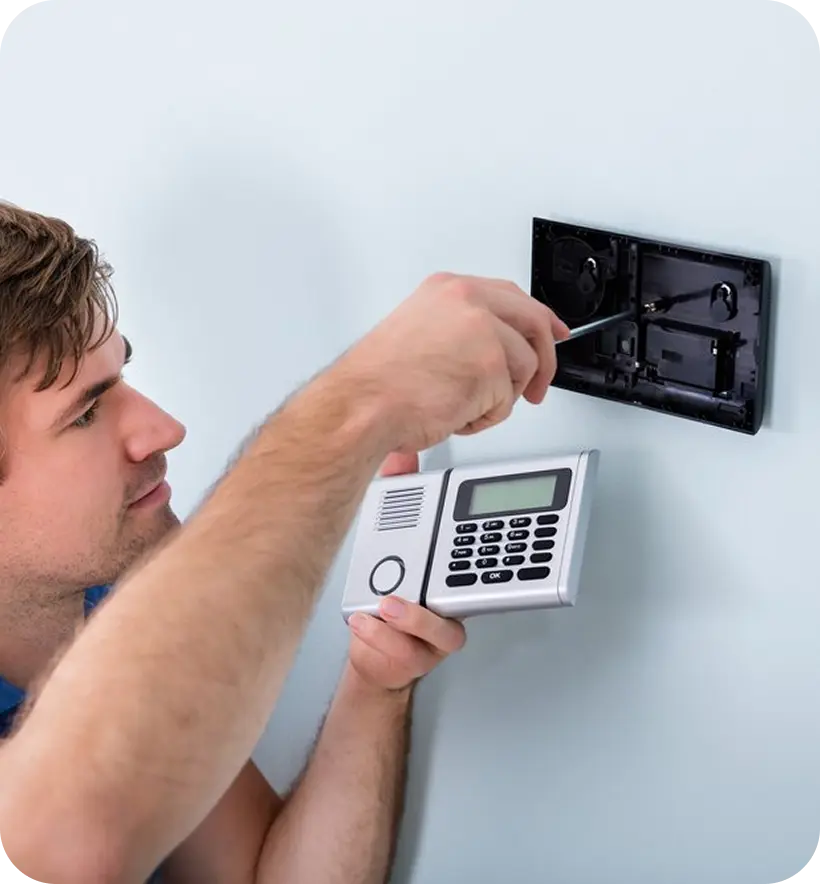 A person installing a wall-mounted intercom system using a screwdriver.