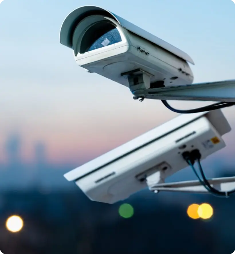 Surveillance cameras mounted on a pole, with a blurred cityscape in the background.