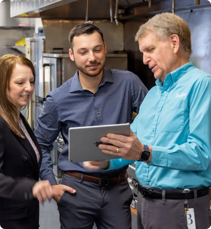 Three people in a kitchen setting looking at a tablet.