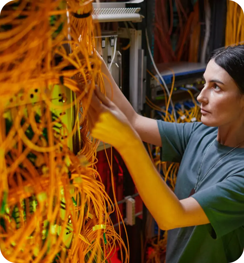 A person in a green shirt is organizing a tangle of orange cables inside a server rack.